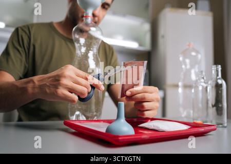 Vista ad angolo basso del contadino maschio che taglia il sacchetto di fertilizzante, prepara i nutrienti per il giardino verticale della torre idroponica, incarna un'agricoltura urbana innovativa Foto Stock