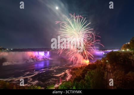 Una spettacolare vista notturna delle Cascate del Niagara, con le Canadian Horseshoe Falls e le American Falls illuminate da vibranti fuochi d'artificio. Foto Stock