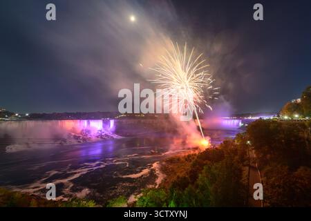 Una spettacolare vista notturna delle Cascate del Niagara, con le Canadian Horseshoe Falls e le American Falls illuminate da vibranti fuochi d'artificio. Foto Stock