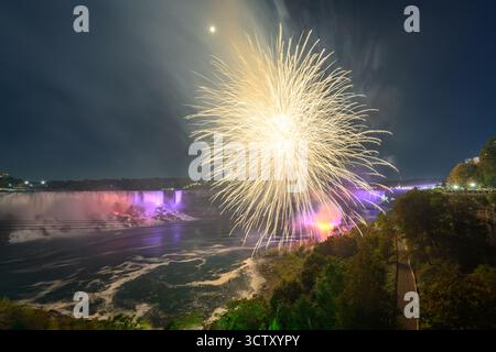 Una spettacolare vista notturna delle Cascate del Niagara, con le Canadian Horseshoe Falls e le American Falls illuminate da vibranti fuochi d'artificio. Foto Stock