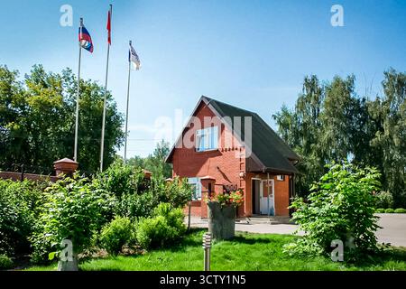 Kolomna, Russia - 17 agosto 2014 - affascinante casa in mattoni rossi con bandiere in un giardino soleggiato. Foto Stock