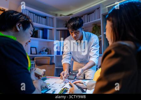 Un team diversificato di professionisti condivide idee su layout architettonici e concetti strutturali, concentrandosi sul lavoro di squadra, la creatività e la precisione in m Foto Stock
