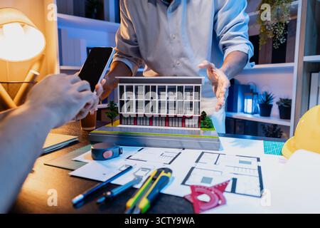 Un team diversificato di professionisti condivide idee su layout architettonici e concetti strutturali, concentrandosi sul lavoro di squadra, la creatività e la precisione in m Foto Stock