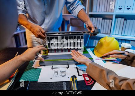 Un team diversificato di professionisti condivide idee su layout architettonici e concetti strutturali, concentrandosi sul lavoro di squadra, la creatività e la precisione in m Foto Stock