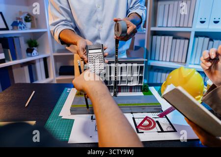 Ingegneri e architetti analizzano i modelli di costruzione e discutono le strategie di progetto, combinando conoscenze tecniche e idee creative per ottenere successo Foto Stock