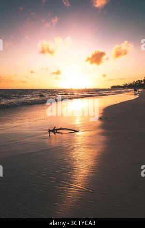 Un bellissimo tramonto dipinge il cielo con colori caldi mentre le onde si infrangono dolcemente contro la riva. La spiaggia di sabbia riflette le vivaci sfumature e cattura la pace Foto Stock