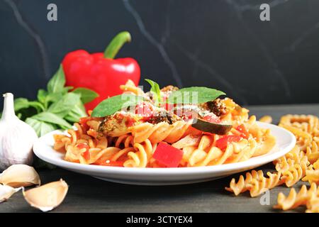 Deliziosa pasta Fusilli di grano intero in salsa di pomodoro con i suoi ingredienti sparsi intorno Foto Stock