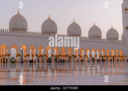 Grande Moschea Sheikh Zayed, Abu Dhabi, Emirati Arabi Uniti, cortile in marmo con archi luminosi, cupole e visitatori, atmosfera serena. Foto Stock
