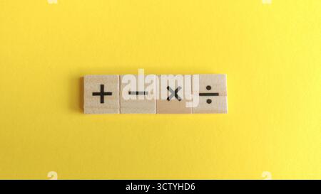 Quattro segnali di funzionamento matematico su blocchi di legno allineati su un sfondo giallo brillante per temi educativi e finanziari. Foto Stock