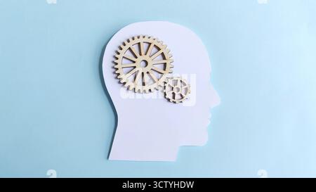 Silhouette della testa umana con ingranaggi in legno interconnessi all'interno, che simboleggiano la meccanica della mente, il pensiero logico, l'innovazione e il processo strategico. Foto Stock