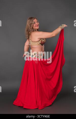 Ballerina felice che guarda la spalla alla alla telecamera, ballando a piedi nudi su sfondo grigio. Vista posteriore di tre quarti della signora in perfor Foto Stock