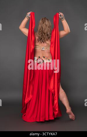 Vista posteriore della modella donna e della ballerina del ventre che indossa un abito da ballo - gonna lunga scarlatta con fessure e senza scarpe o calze, esibendosi con i Foto Stock