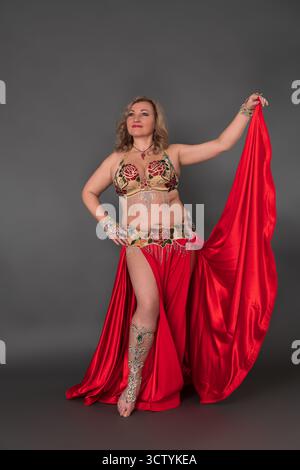 Bella modella di moda e ballerina del ventre che indossa in costume da ballo - gonna lunga bralette e cremisi con fessura, si muove a piedi nudi in pieno lengt Foto Stock