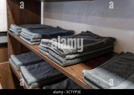 Asciugamani grigi ben piegati impilati su un ripiano di legno all'interno dello spogliatoio pubblico o dell'area spogliatoio della palestra Foto Stock