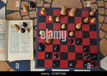 Guardando in basso sul campo di battaglia di un'apertura di scacchi. Imparare a pensare, pianificare e strategia con un libro di scacchi e set di scacchi e scacchiere d'epoca Foto Stock
