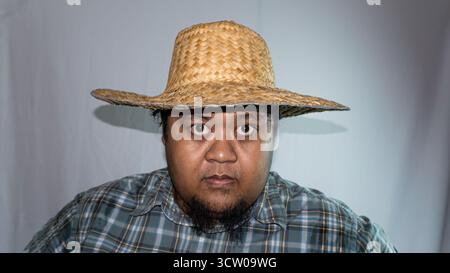 Uomo indonesiano che indossa un cappello di paglia e una camicia a scacchi verde su sfondo bianco. Foto Stock