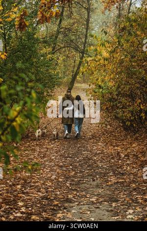 Coppia che cammina con i cani attraverso il sentiero autunnale Foto Stock
