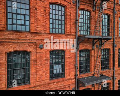 Primo piano della facciata della fabbrica di mattoni rossi a Lodz, Polonia, con scalinata in metallo nero e grandi finestre, composizione di luce diurna HDR per architettura, educati Foto Stock
