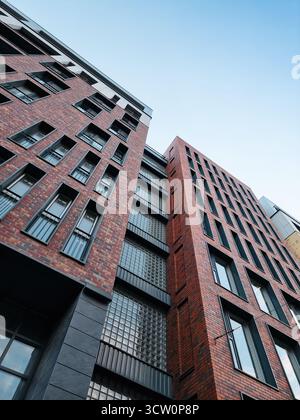 Si affaccia su di un edificio moderno con facciata in mattoni e blocchi di vetro. Elegante edificio residenziale che si affaccia sul cielo azzurro. Foto Stock
