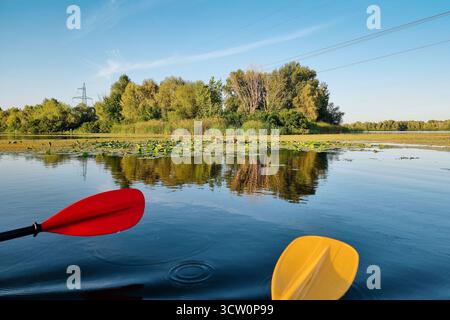 Kayak rosso e giallo pagaiano sulla superficie dell'acqua su un lago. POV in prima persona: Nuoto in kayak tandem in una giornata di sole. Foto Stock