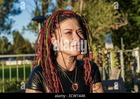 Donna con dreadlock rossi e verdi che indossa un top nero lucido e una collana a cuore rosso Foto Stock