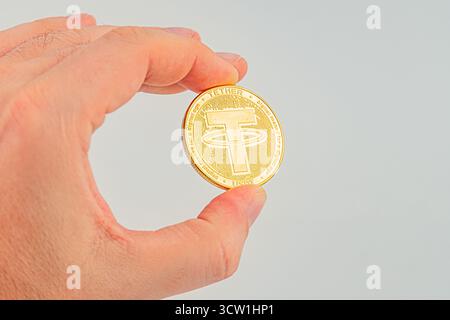 Una mano tiene una moneta Tether su un fondo semplice, simboleggiando la ricchezza o l'investimento in criptovaluta moneta Tether a Foto Stock