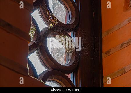 Una tradizionale finestra in vetro colorato con intricati motivi circolari e linee ondulate, che proiettano ombre e luci, simboleggiano la tranquillità e lo storico Foto Stock