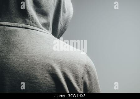 Uomo irriconoscibile con felpa con cappuccio grigio chiaro visto da dietro in condizioni di scarsa illuminazione, concetto di solitudine, segretezza e identità nascosta. Messa a fuoco selettiva. Foto Stock