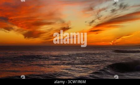 Vista aerea di un tramonto ardente che si illumina sulle onde scure dell'oceano, una sinfonia di arancione e nero vicino alla costa, città del Capo, Capo Occidentale, Sud Africa. Foto Stock