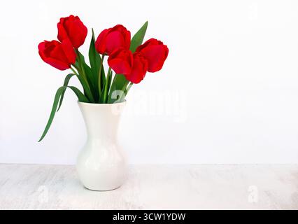 Bouquet di fiori di tulipani rossi in vaso bianco di porcellana su un tavolo bianco con spazio per il testo Foto Stock