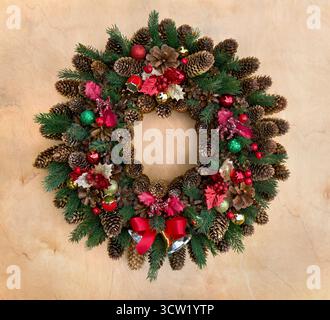 Decorazione natalizia. Corona di Natale di abete rosso, pino a coni, albero di natale ramificato, agrifoglio rosso, campane e palle su sfondo di legno Foto Stock