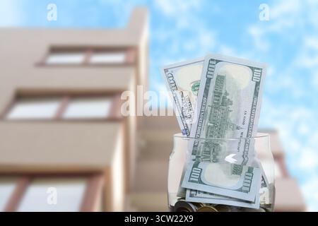 Barattolo con dollari e monete contro il condominio. Risparmiare denaro per comprare un appartamento Foto Stock