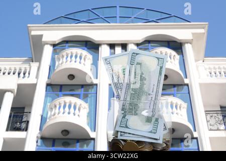 Barattolo con dollari e monete contro il condominio. Risparmiare denaro per comprare un appartamento Foto Stock