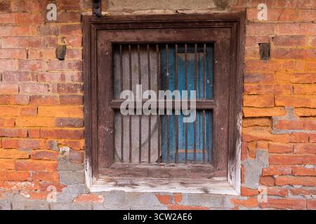 Primo piano di un vecchio muro con mattoni irregolari, cemento grezzo e una cornice arrugginita della finestra che mostra una struttura resistente agli agenti atmosferici e degrado urbano. Foto Stock