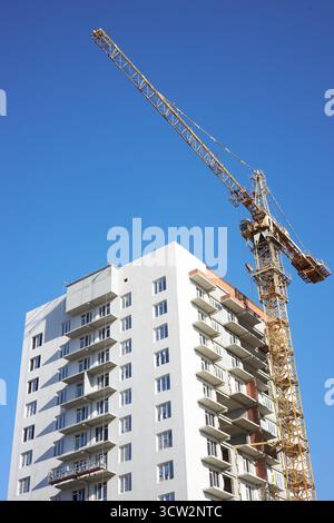 la gru da cantiere è posizionata accanto a un alto edificio in costruzione. I lavoratori possono essere visti sul sito, preparandosi per le prossime fasi del progetto Foto Stock
