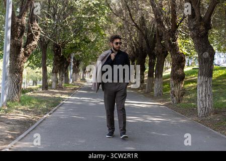 Un uomo sta camminando lungo un sentiero alberato con una giacca posta sulle spalle Foto Stock