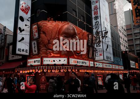 Il negozio di un ristorante kushikatsu nel quartiere Shinsekai di Osaka, caratterizzato da un volto gigante e da lanterne luminose che attirano visitatori curiosi Foto Stock