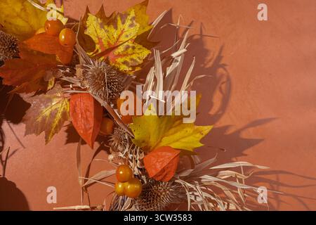Primo piano di foglie floreali essiccate e di foglie autunnali su sfondo arancione. Arredamento autunnale e concetto per il giorno del Ringraziamento Foto Stock