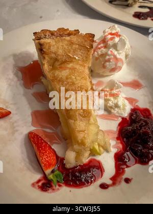 Fetta di strudel di mele con gelato alla vaniglia, confettura di fragole e fragola fresca su un piatto in un ristorante Foto Stock