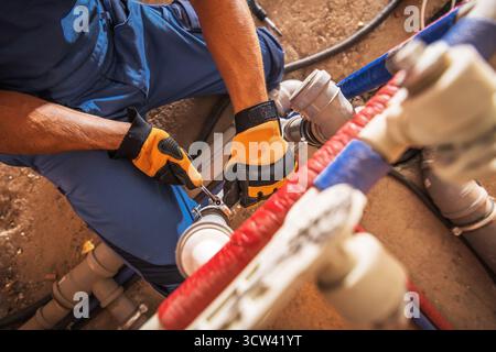 Un idraulico utilizza strumenti per riparare i sistemi di tubazioni in un ambiente di costruzione, mostrando il lavoro pratico e le capacità di risoluzione dei problemi nelle riparazioni idrauliche. Foto Stock
