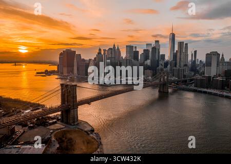 Vista aerea dell'iconico Ponte di Brooklyn che si estende verso i grattacieli torreggianti della città sotto un cielo abbronzato di ardenti tonalità del tramonto, New York, New York, Stati Uniti. Foto Stock