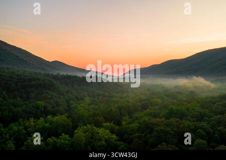 Vista aerea della lussureggiante e verde tettoia del Parco Nazionale dello Shenandoah che incontra le valli nebbiose mentre il sole dipinge il cielo con sfumature ardenti, Shenandoah, Virginia, Stati Uniti. Foto Stock