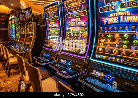 Oceano Atlantico - 28 settembre 2025, fila colorata di slot machine illuminate all'interno del casinò della nave da crociera Enchanted Princess, con sedie ordinate Foto Stock
