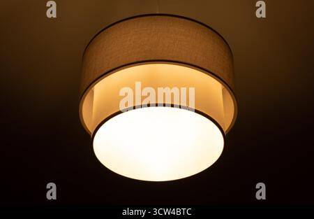 Lampada luminosa accesa in un paralume rotondo, illuminazione interna su sfondo scuro Foto Stock