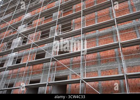 Costruzione di ponteggi di un edificio a piu' piani in mattoni rossi. l'edificio e' in costruzione, ponteggi in metallo collocati all'esterno di un appartamento infinito Foto Stock