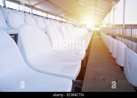 Posti vuoti bianchi di tribuna sullo stadio sportivo. Molti posti vuoti in plastica in fila in uno stadio all'aperto. Concetto di fan, sedie per il pubblico Foto Stock