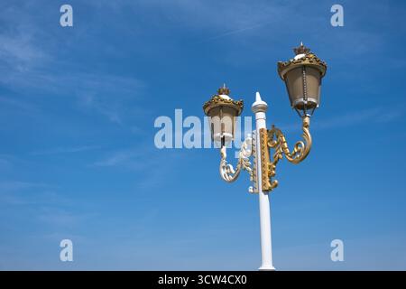 Lampione da strada bianco e oro decorato contro un cielo blu chiaro Foto Stock