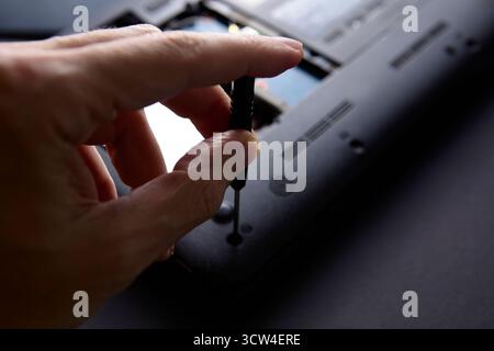 Una mano regge un cacciavite svitando il pannello posteriore di un computer portatile durante un processo di riparazione. La scena mette in evidenza la manutenzione della tecnologia e il re tecnico Foto Stock