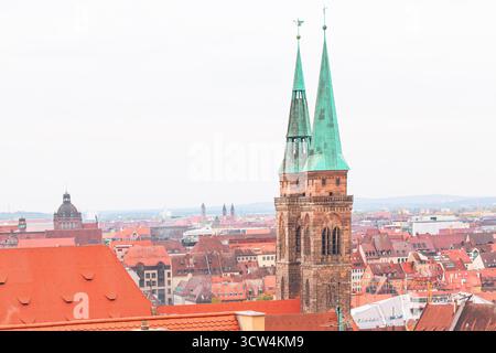 Chiesa di San Sebaldo con guglie verdi distintive, che si innalzano sopra gli edifici dal tetto rosso della città vecchia di Norimberga. L'immagine acquisisce una vista classica Foto Stock