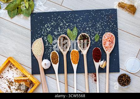 Spezie e condimenti assortiti su cucchiai di legno. Una varietà di spezie colorate, erbe aromatiche e condimenti disposti su cucchiai di legno su sfondo scuro Foto Stock